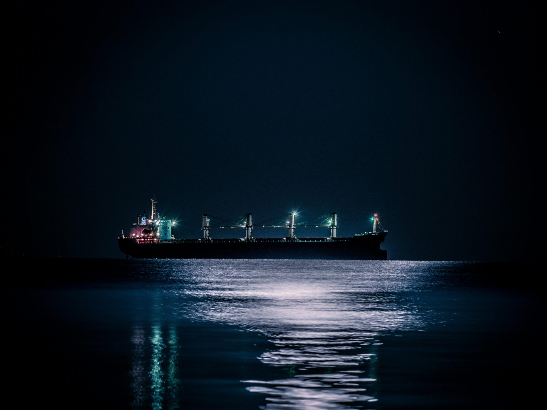 A tranquil nighttime scene of a cargo ship floating on a calm ocean under a starlit sky.