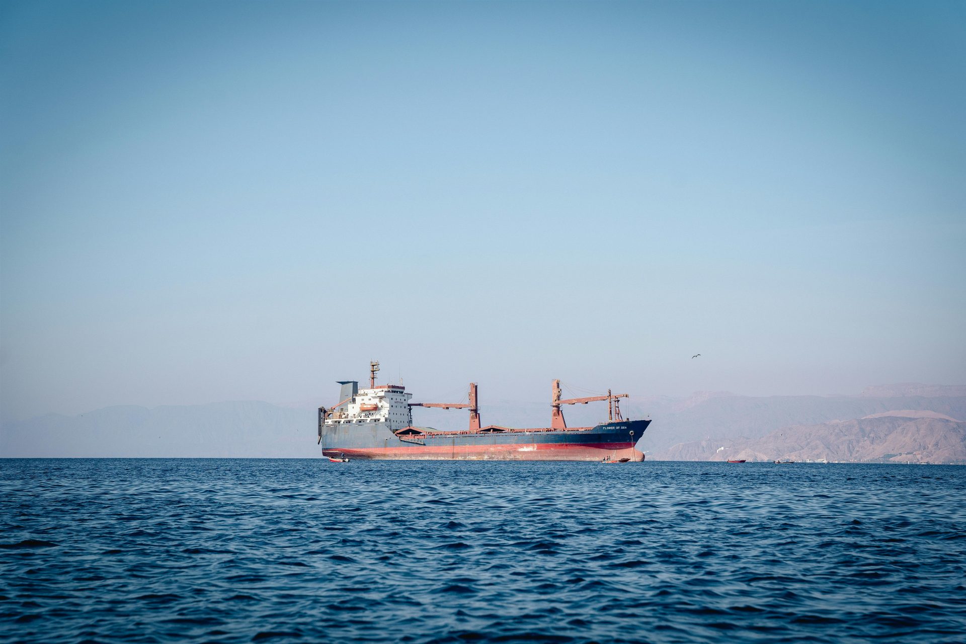 A cargo ship sailing on calm ocean waters under a clear blue sky.